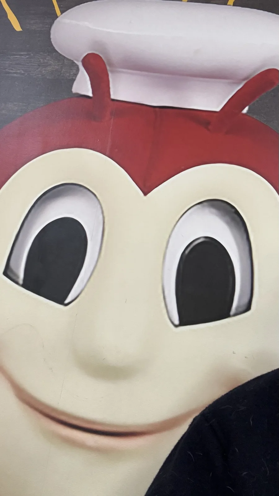 A close-up of a cartoonish mascot with a red head, white chef's hat, large black eyes, and a smiling face, overlaid with the…