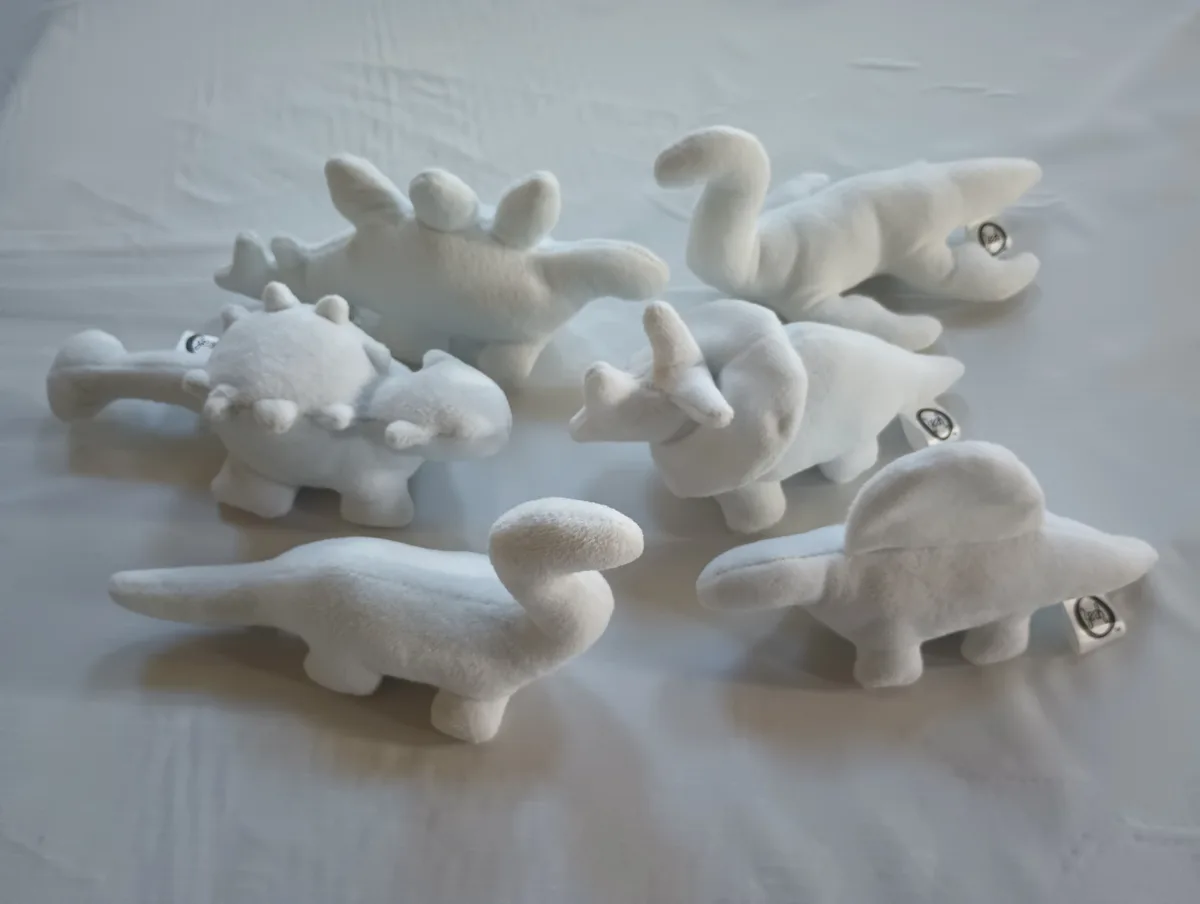Several white plush dinosaur toys of various species are arranged on a white fabric surface. The overlaid text reads 'i'm…