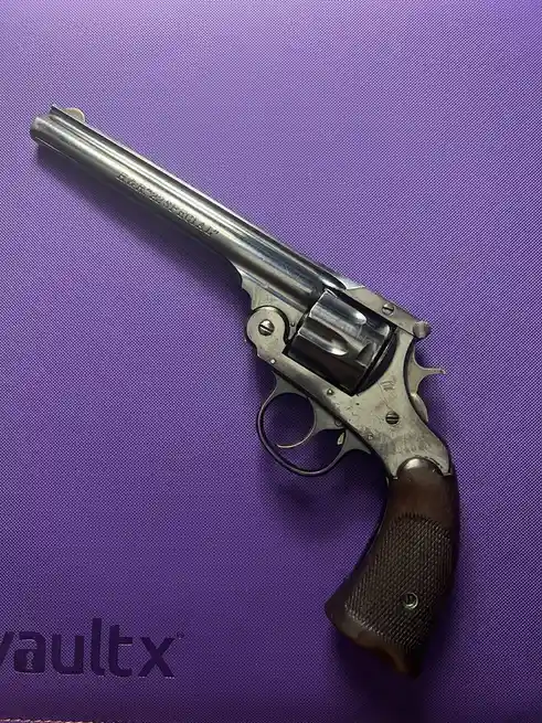 A silver H&R .22 Special revolver with a wooden grip rests diagonally on a textured purple surface, which has the partial…
