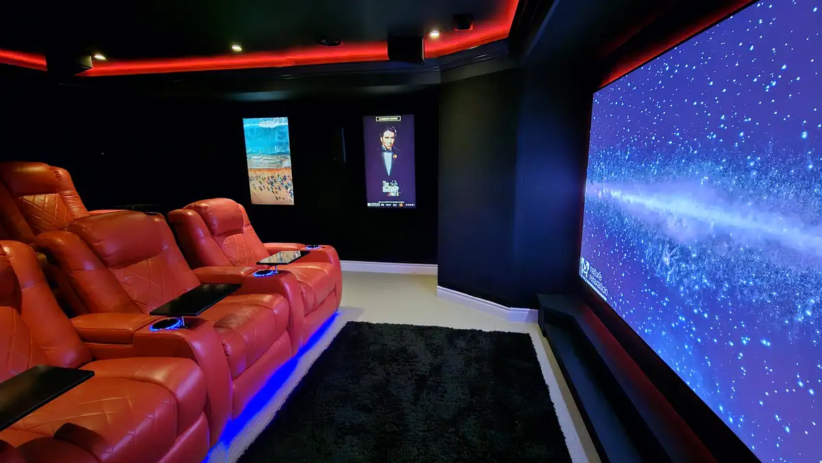 A luxurious home theater with red leather recliners, a large screen showing a starfield, and a smaller screen displaying a…