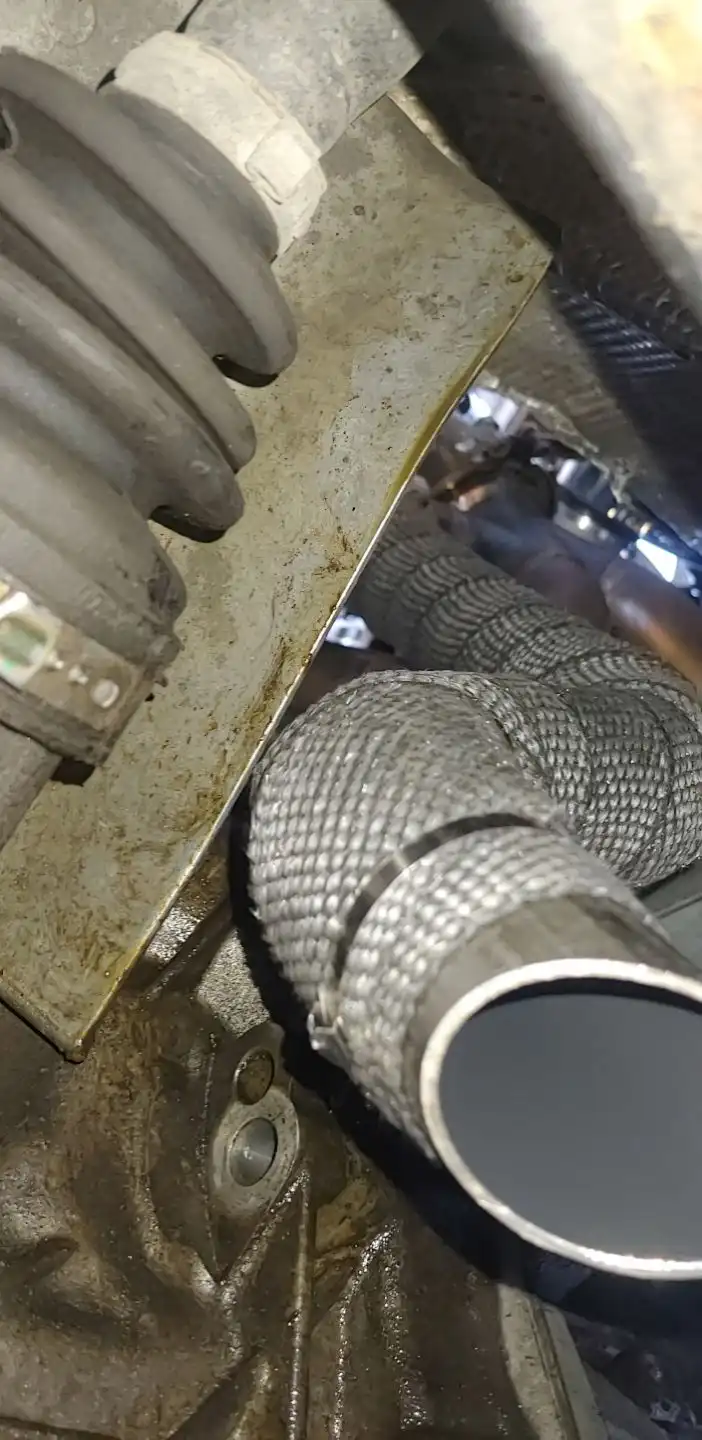 A close-up photo of a car's undercarriage showing a newly installed metallic mesh exhaust pipe, with surrounding dirty metal…