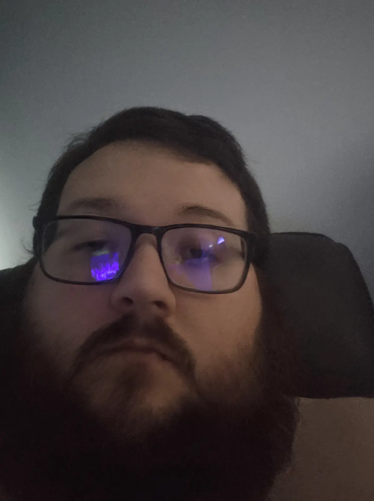 A close-up selfie of a man with a beard and glasses, looking directly at the camera with a neutral expression. His glasses…