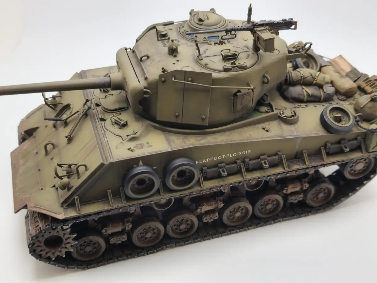 A highly detailed scale model of a military tank, painted in olive drab with weathering effects, is photographed against a…