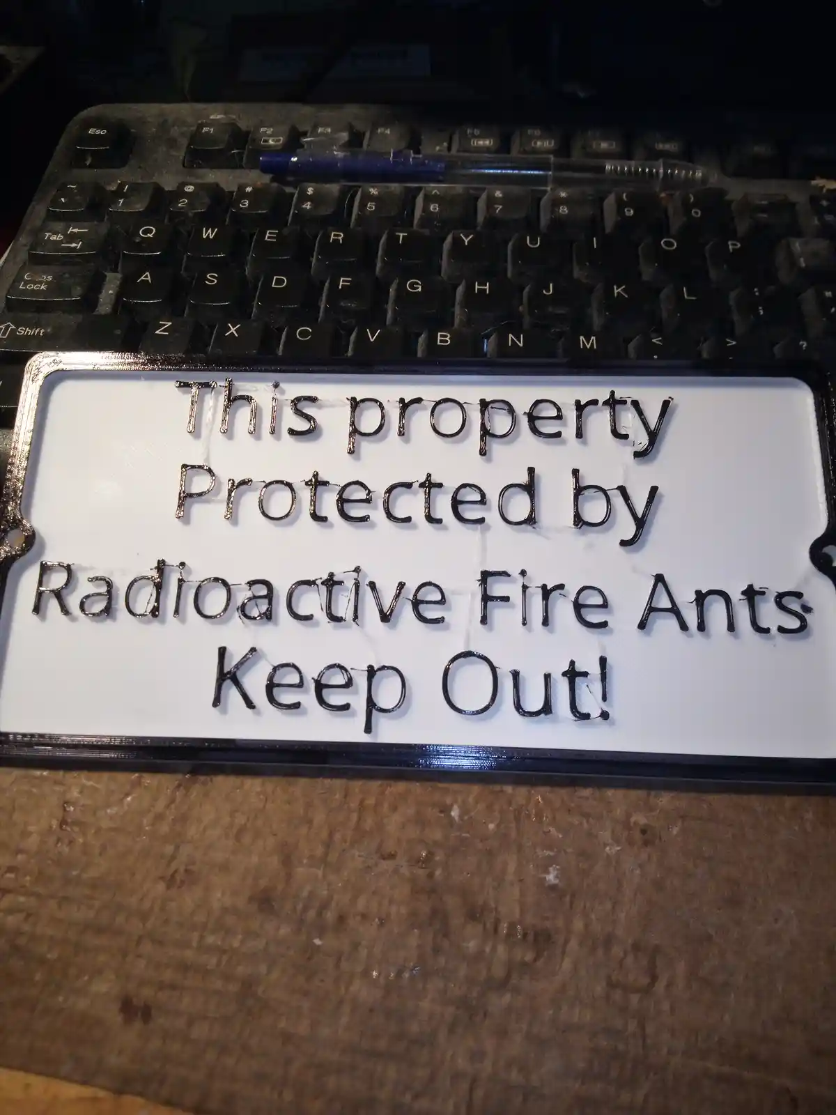 A white rectangular sign with black text reading 'This property Protected by Radioactive Fire Ants Keep Out!' is placed on a…
