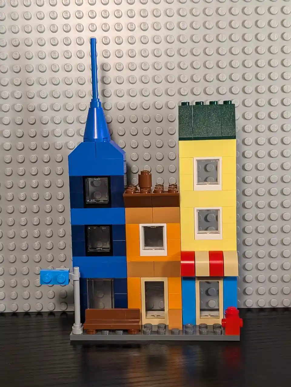 A colorful Lego building constructed from various bricks, featuring a blue tower with a spire, an orange section, and a…