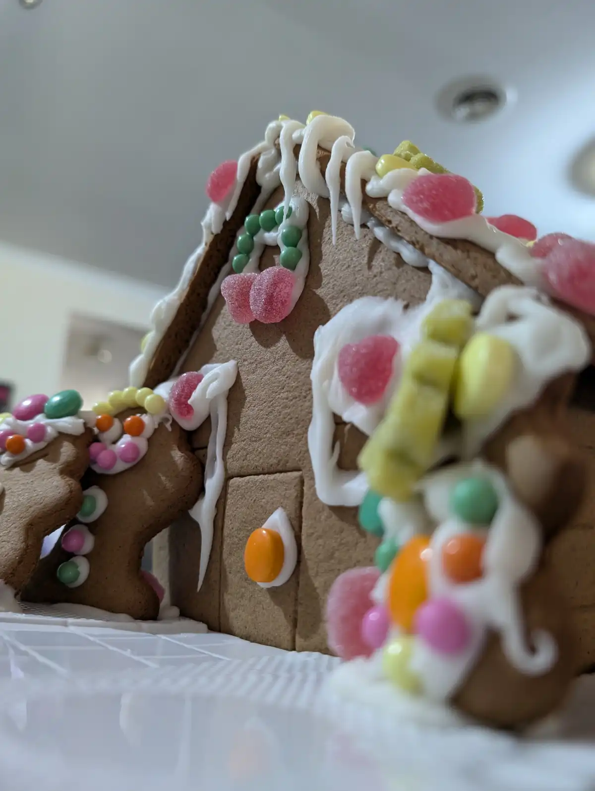 A close-up photo of a gingerbread house decorated with white icing, pink and green candy, and colorful gumdrops. The text…