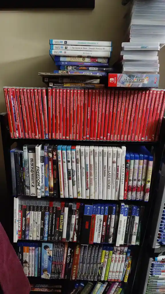 A tall black shelf is densely packed with video game cases and anime DVDs/Blu-rays from various consoles like Wii, Wii U…