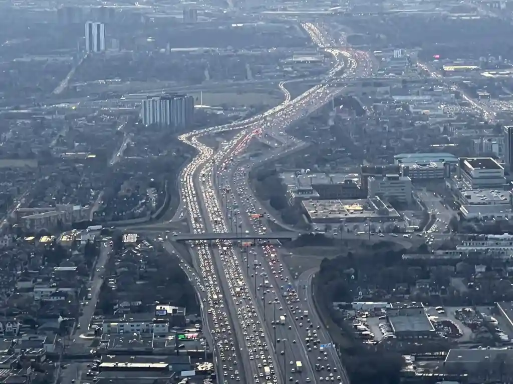 An aerial view of a massive, multi-lane highway choked with dense traffic, stretching through a sprawling urban area with…