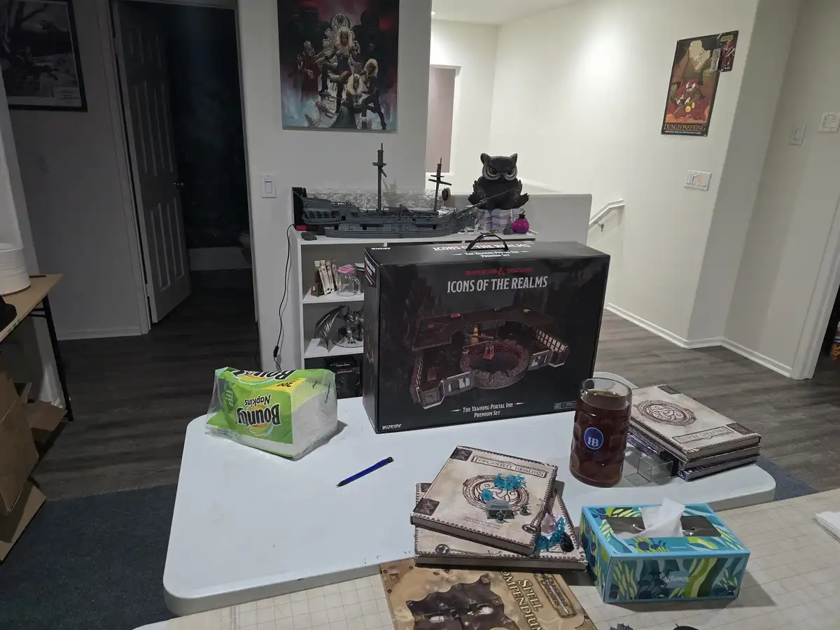 A white table is cluttered with Dungeons & Dragons gaming supplies, including a large 'Icons of the Realms' box, spellbooks…