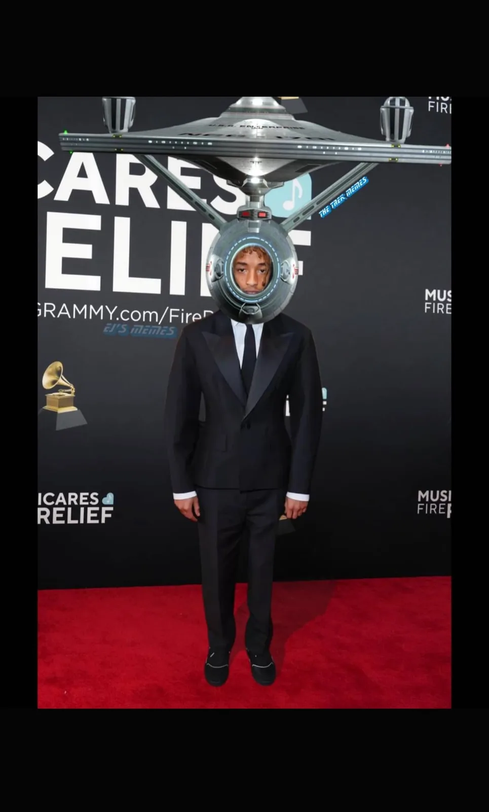 A man in a black tuxedo stands on a red carpet at a Grammys event, but his head has been replaced with a Star Trek…