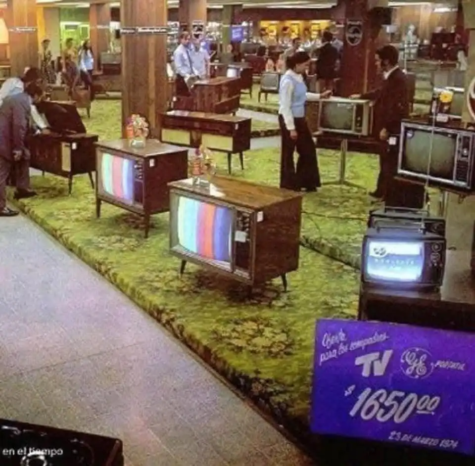 A vintage 1974 photo shows a crowded electronics store with numerous retro wooden televisions on display, some showing test…