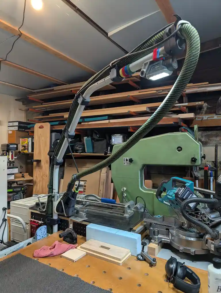 A cluttered woodworking workshop features a complex, custom-built robotic arm with a flexible hose and a bright LED light…