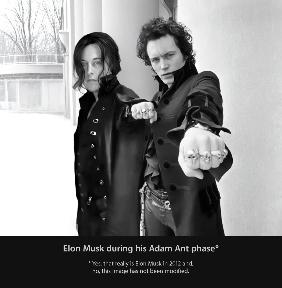 A black and white photo shows two men in dramatic, dark, 1980s-style costumes with skull rings, posing with fists forward…