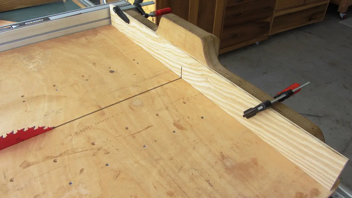A woodworking project shows a table saw with a custom wooden fence attached, clamped securely to the table. The fence has a…