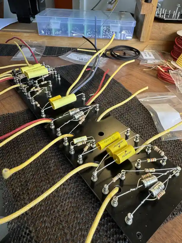 A close-up photo of a messy, hand-wired electronic circuit board with numerous yellow and red wires, capacitors, and…