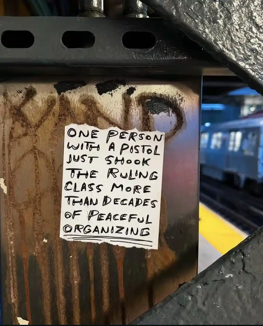 A torn piece of white paper with handwritten black text is stuck to a rusty metal pole in a subway station. The text reads…