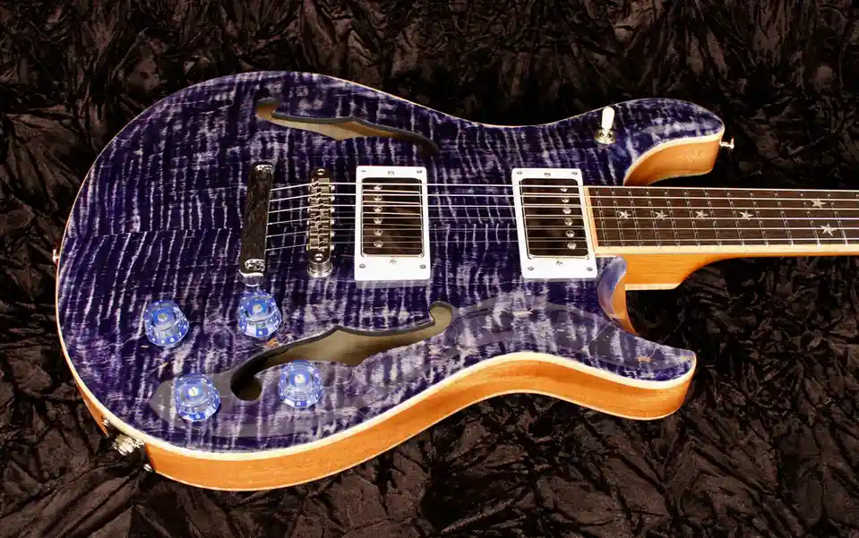 A close-up photo of a purple and white flame maple finish electric guitar with a double-cutaway body, silver pickups, and…