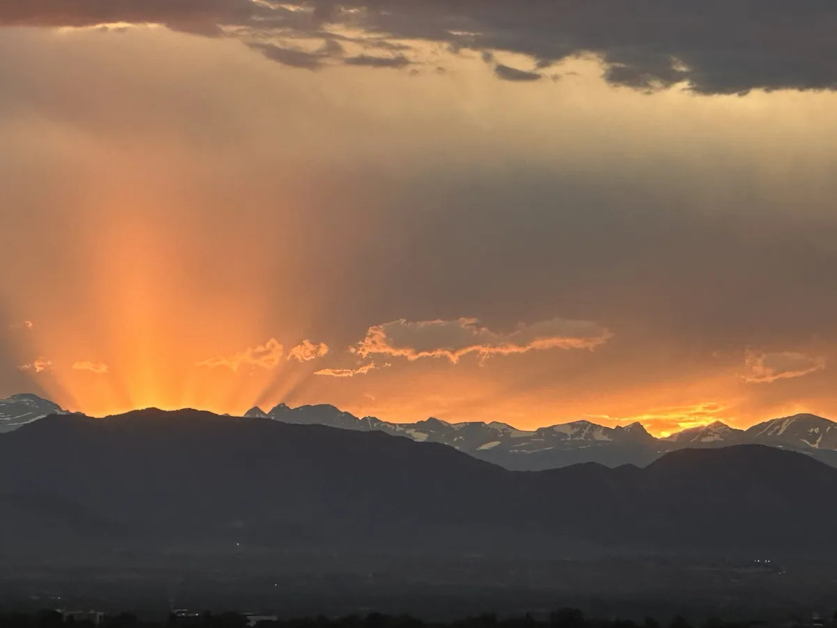 A dramatic landscape photo shows a mountain range silhouetted against a vibrant sunset or sunrise, with bright orange…