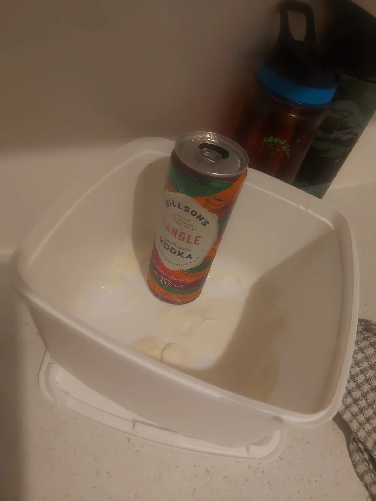 A can of Billson's Tangle Vodka sits upright in a white plastic container filled with a white, milky liquid, likely milk…