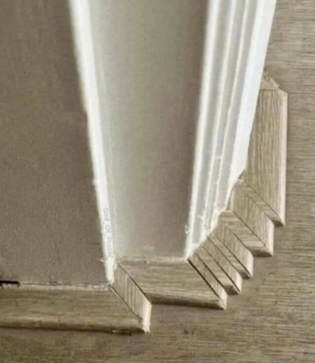 A close-up photo shows a white baseboard meeting a wooden floor at a corner, where the baseboard is visibly damaged and…
