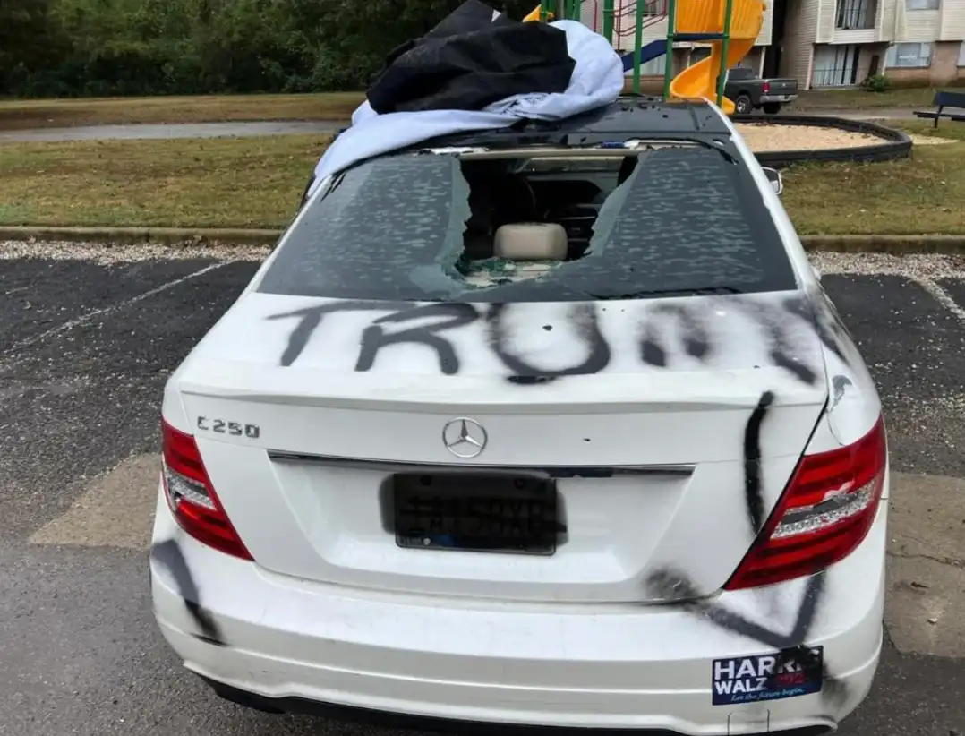The rear of a white Mercedes-Benz C250 is shown with its rear window shattered and spray-painted with the word 'TRUMP'…