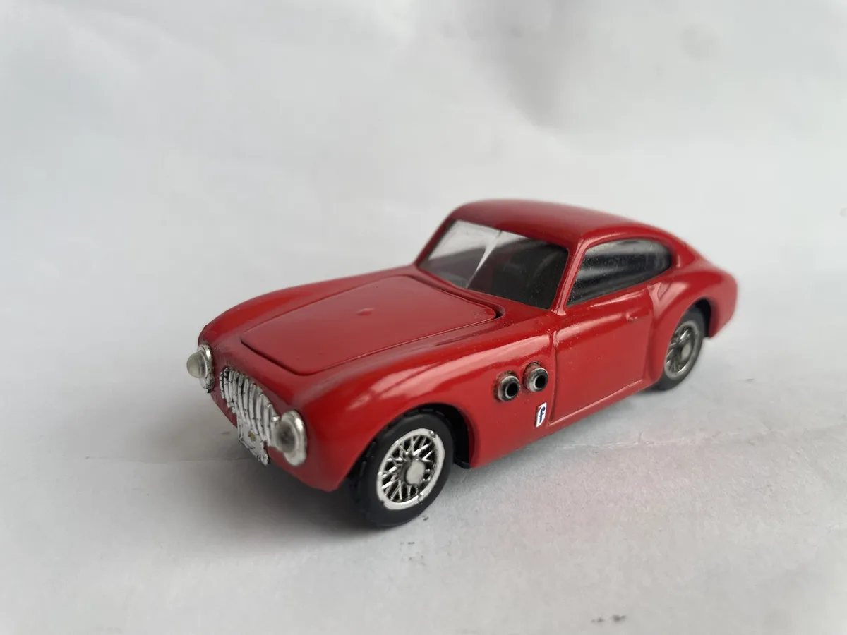 A red toy car model is photographed against a plain white background. The car has a classic design with silver wheels and a…