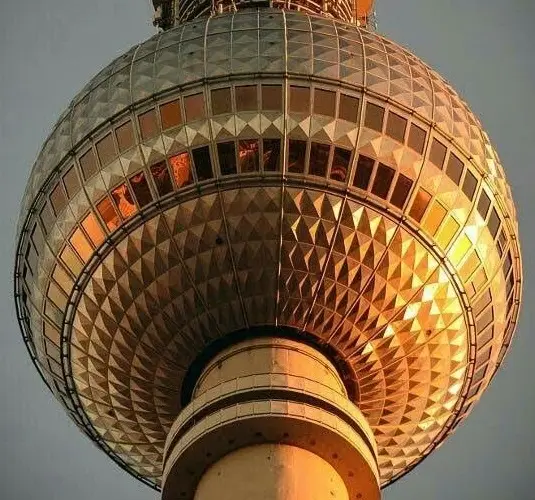 A low-angle photo of the Berlin TV Tower's iconic spherical observation deck, illuminated by golden sunset light reflecting…