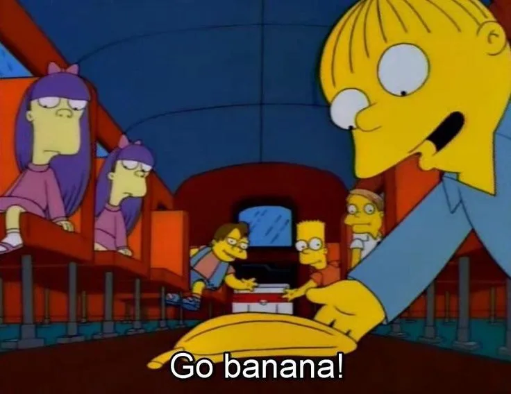 A still from The Simpsons shows a large yellow character with a banana-shaped head, smiling and pointing down at a banana on…