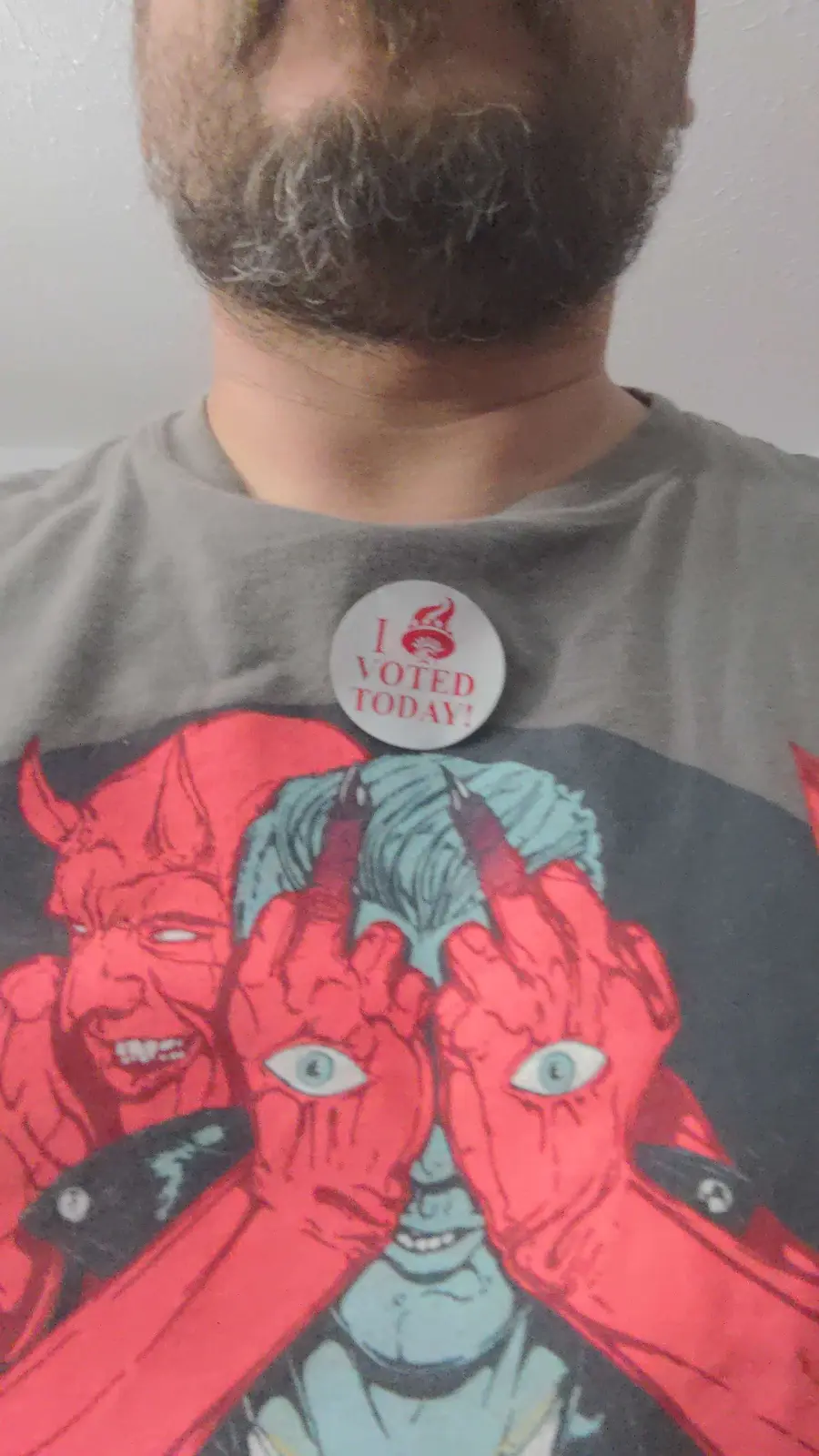 A person with a beard wears a gray t-shirt featuring a graphic of the comic book character Hellboy, who has red skin, horns…