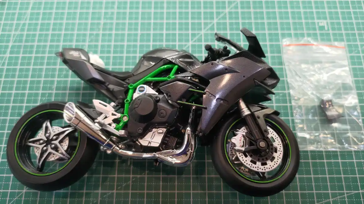 A detailed scale model of a black and green sport motorcycle with chrome exhaust and silver wheels sits on a green grid…