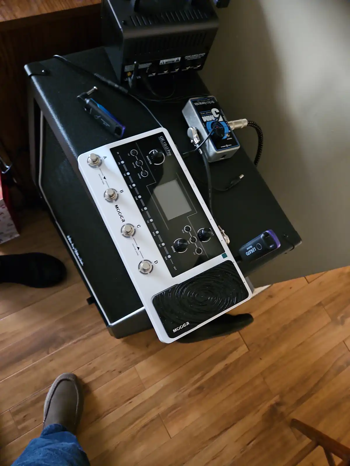A white Moogerfooger OF-150 Pro effects pedal sits atop a black guitar amplifier, surrounded by other pedals and cables. A…