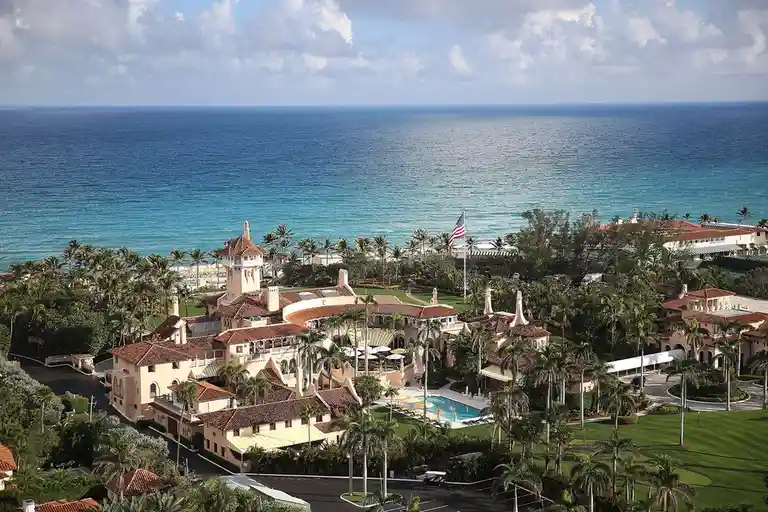 An aerial view of a luxurious, sprawling resort complex with terracotta roofs, palm trees, and a large pool, situated…