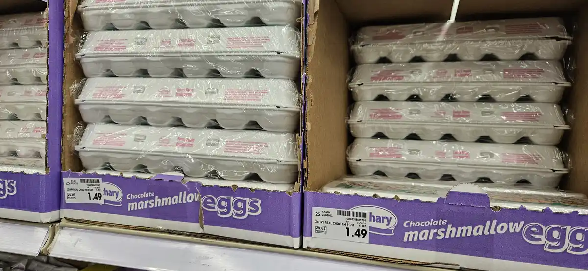 Two boxes of chocolate marshmallow eggs are stacked on a store shelf, each containing multiple plastic-wrapped cartons. The…