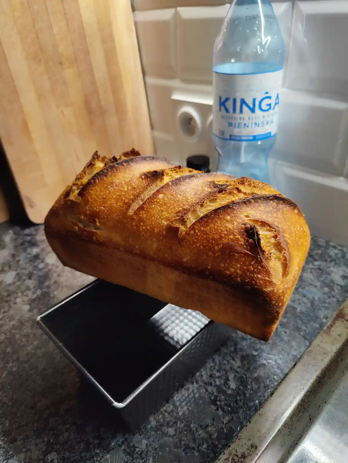 A freshly baked loaf of bread with a golden-brown crust and scored top is suspended mid-air, seemingly floating above its…