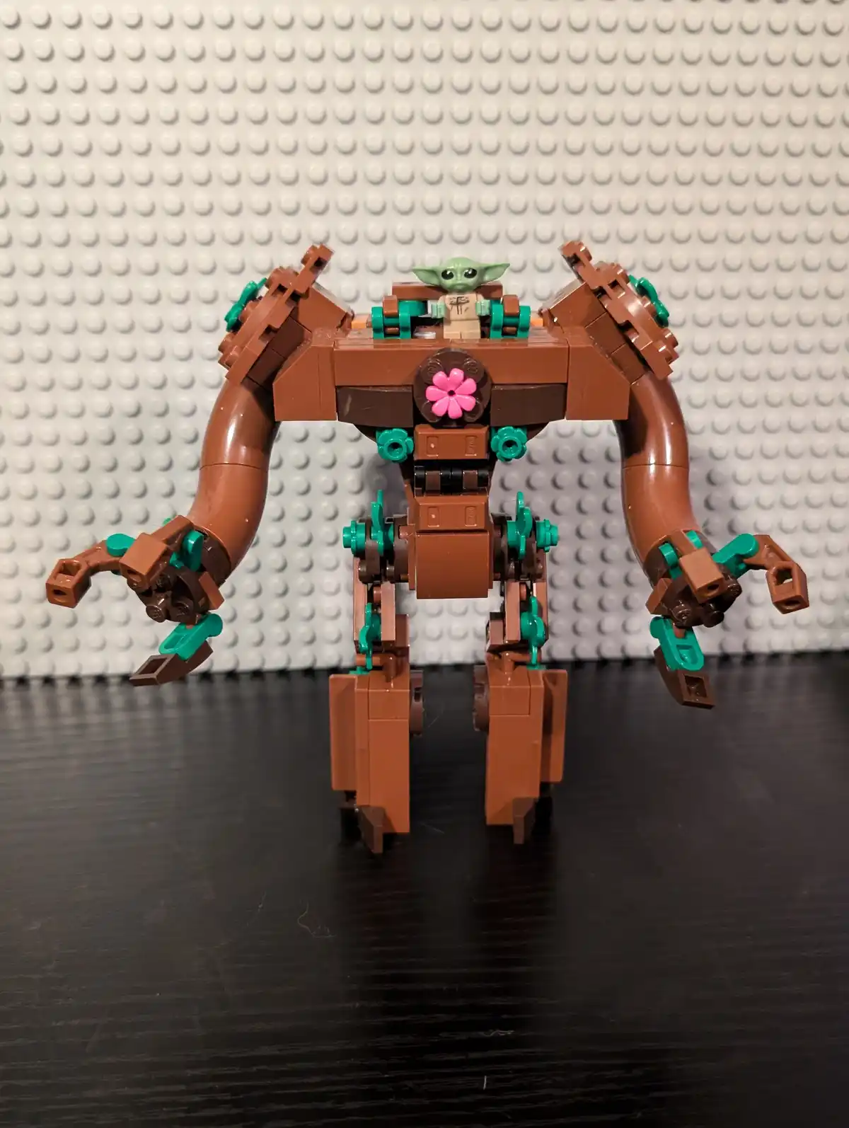 A LEGO model of Grogu (The Child) from Star Wars sits atop a large, brown, mechanical walker with teal joints and a pink…