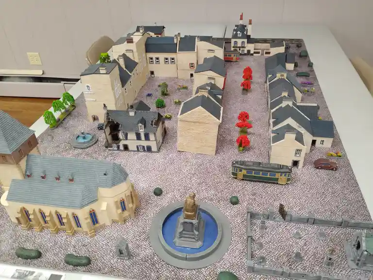 A detailed scale model of a European-style town with cobblestone streets, miniature buildings, a church, a fountain with a…
