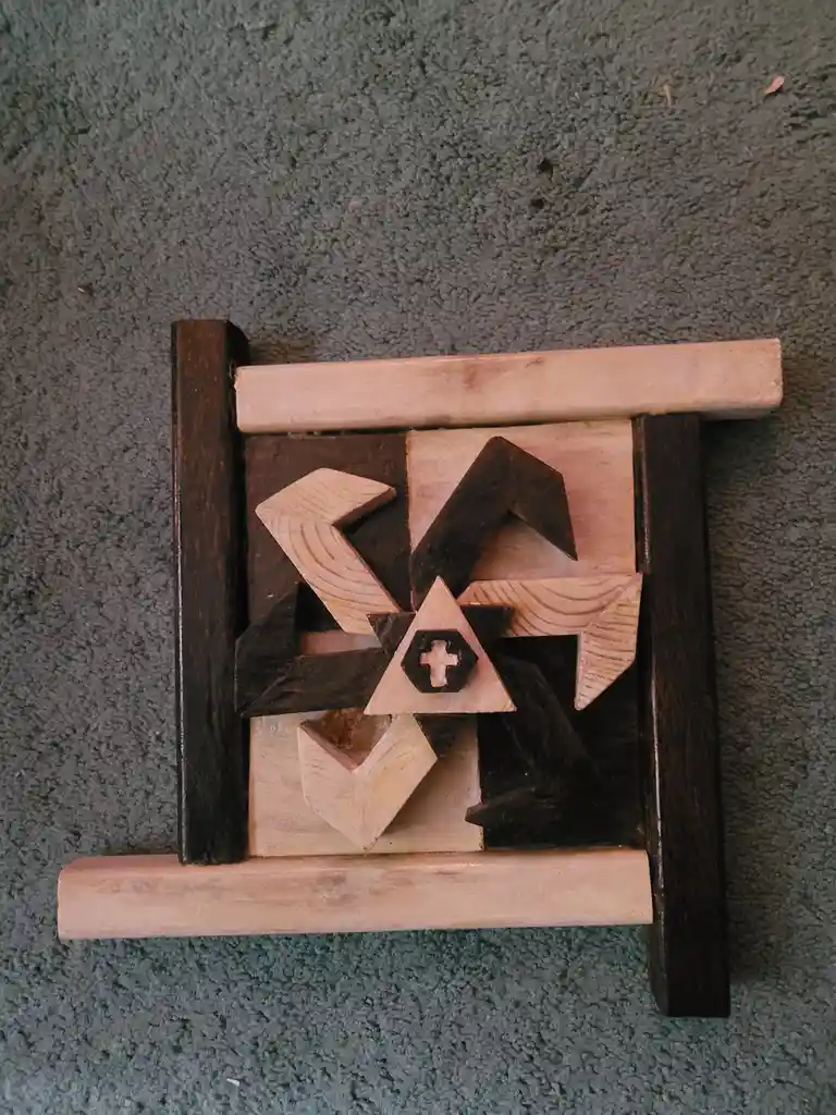 A wooden puzzle with interlocking geometric pieces in light and dark wood sits on a gray carpet. The central piece is a…