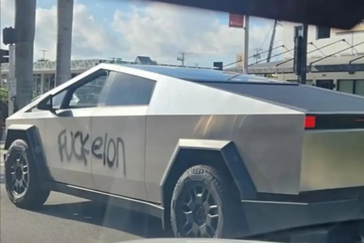 A silver Tesla Cybertruck is shown parked outdoors with the phrase 'fuck elon' spray-painted in black graffiti across its…