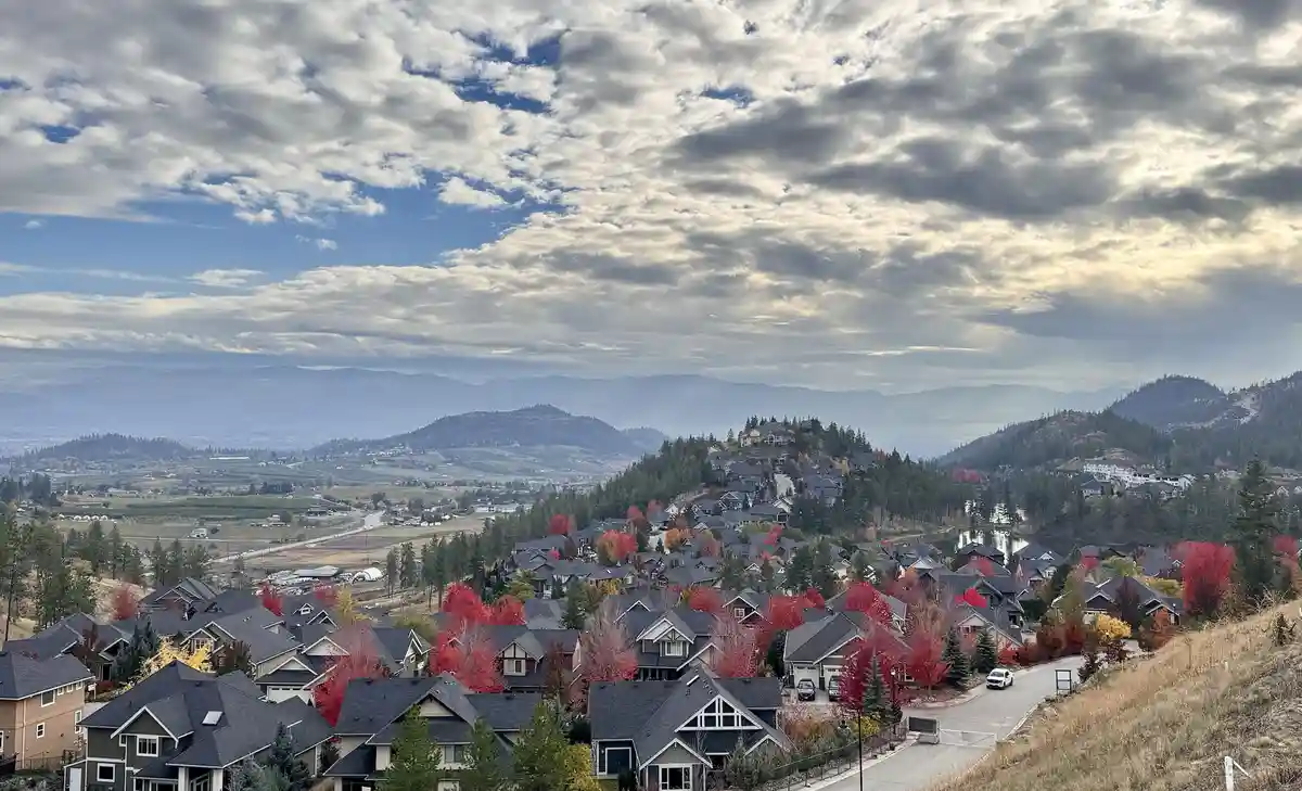 A scenic photo of a suburban neighborhood on a hillside with autumn-colored trees under a cloudy sky, overlaid with the text…
