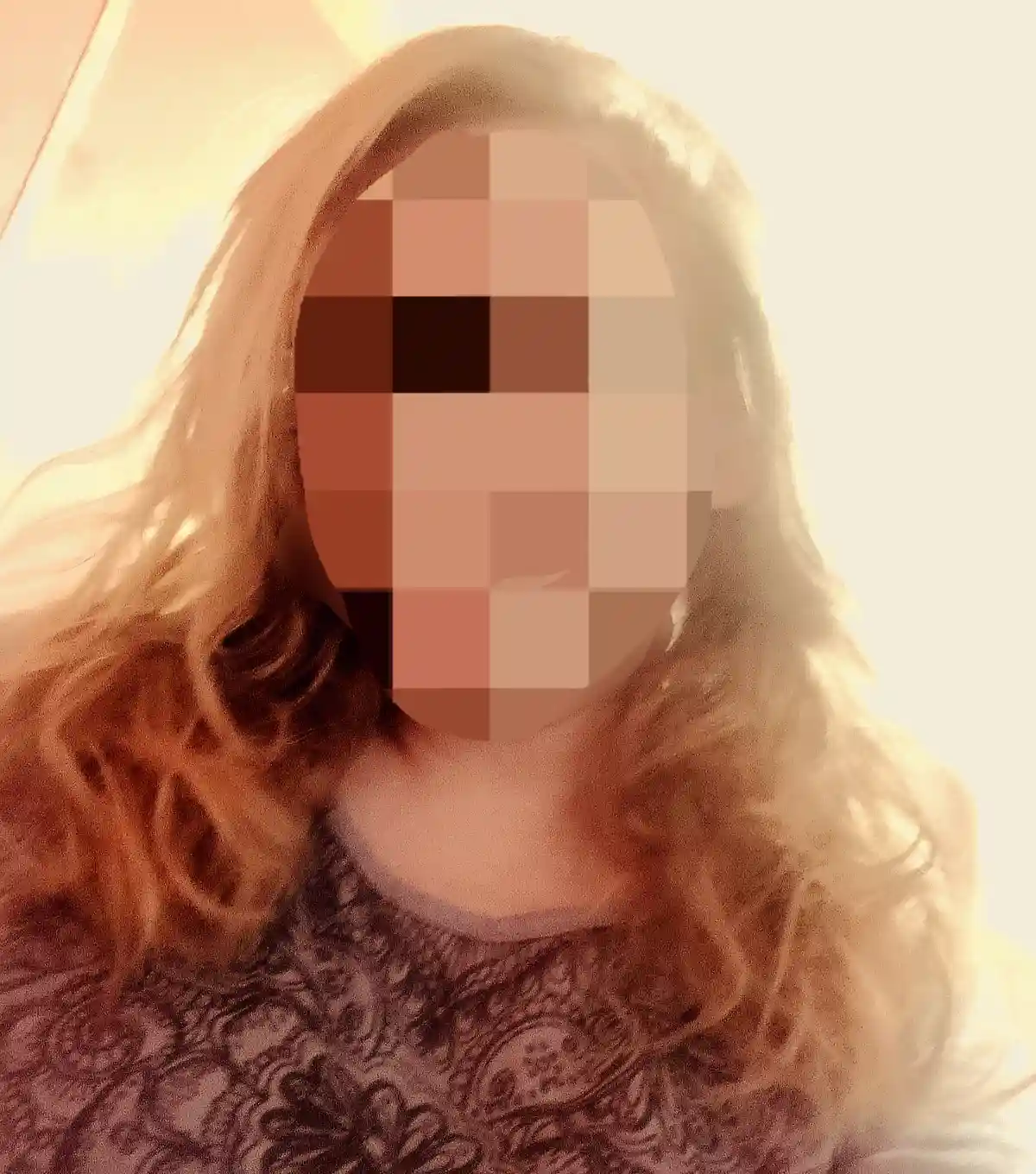 A person with long, wavy, light-brown hair is shown from the shoulders up, wearing a dark, patterned top. Their face is…