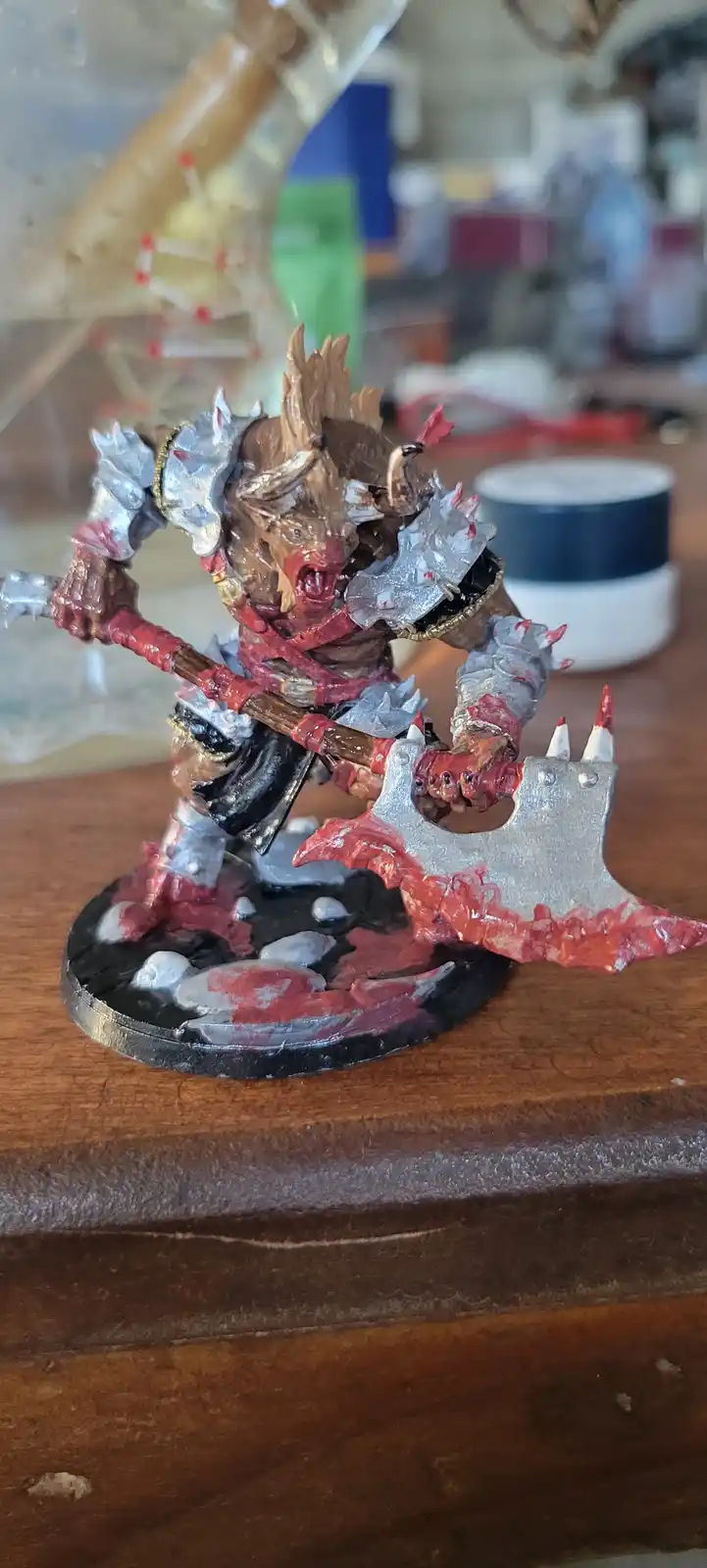 A hand-painted fantasy miniature of a monstrous, horned warrior with silver armor and a large axe, standing on a wooden…