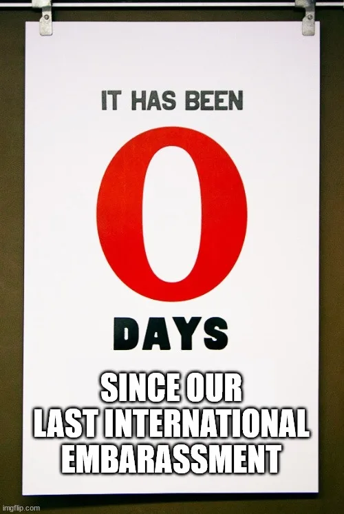 A white poster with bold text reads 'IT HAS BEEN 0 DAYS SINCE OUR LAST INTERNATIONAL EMBARASSMENT', featuring a large red…
