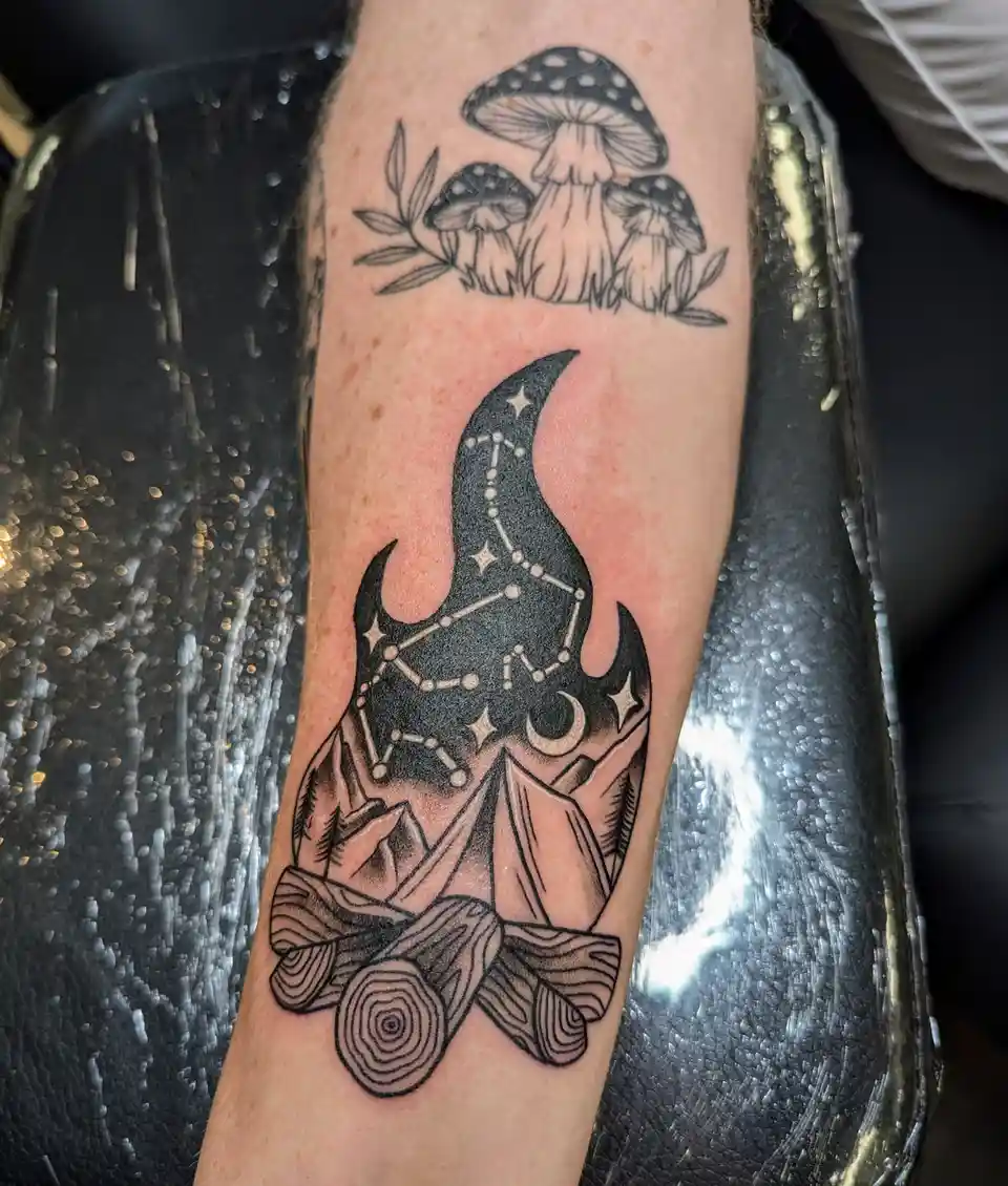 A close-up of a person's forearm showing two tattoos: the top one depicts three spotted mushrooms with leaves, and the…