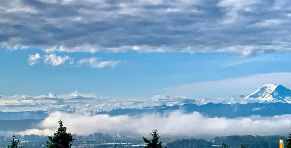 A scenic landscape photo shows a snow-capped mountain peak rising above a sea of clouds, with a blue sky and scattered…