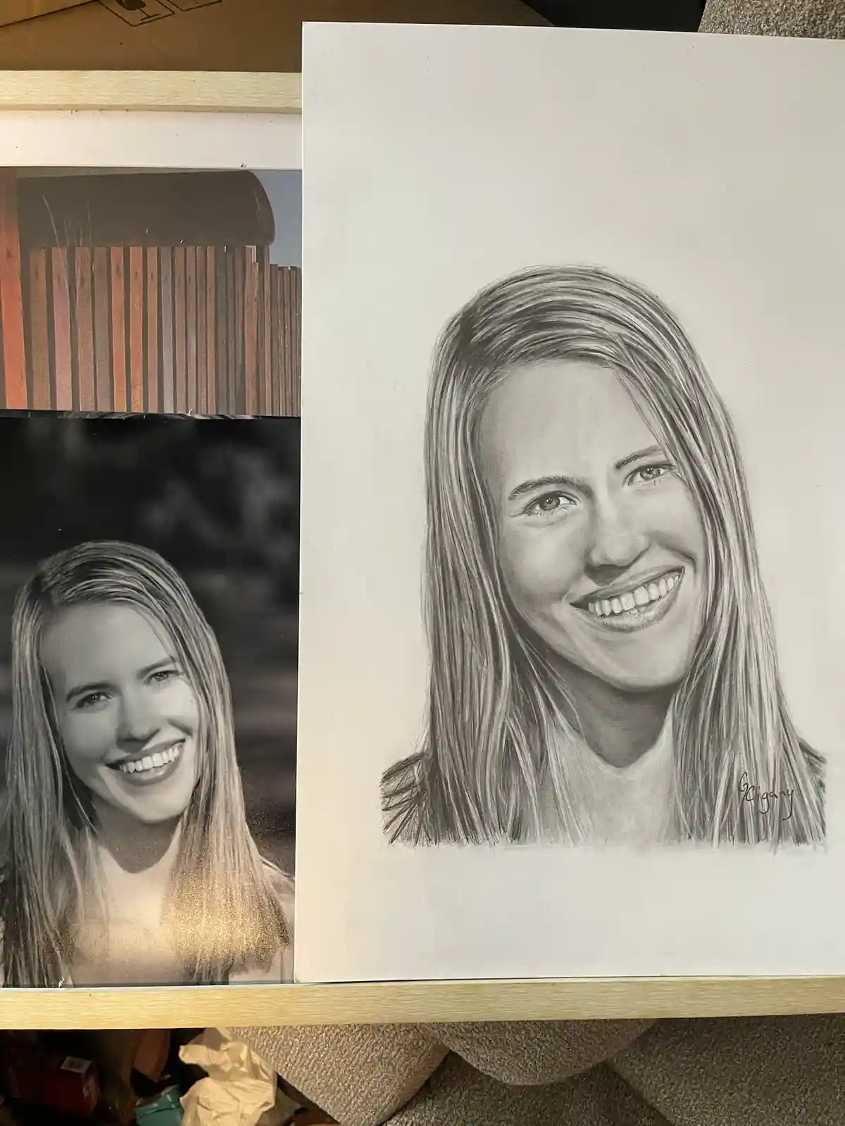 A black-and-white pencil portrait of a smiling woman with long hair is displayed next to a reference photo of the same…