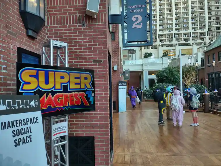 A photo from the Super MagFest convention shows a colorful 'SUPER MAGFEST' sign on a brick wall next to a 'MAKERSPACE SOCIAL…