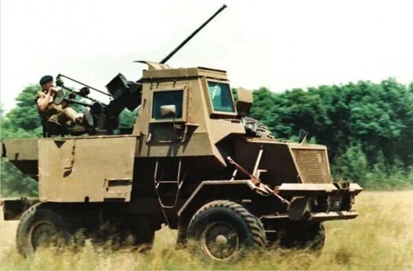 A tan armored military vehicle with a mounted anti-aircraft gun is shown in a grassy field. A soldier sits in the open…