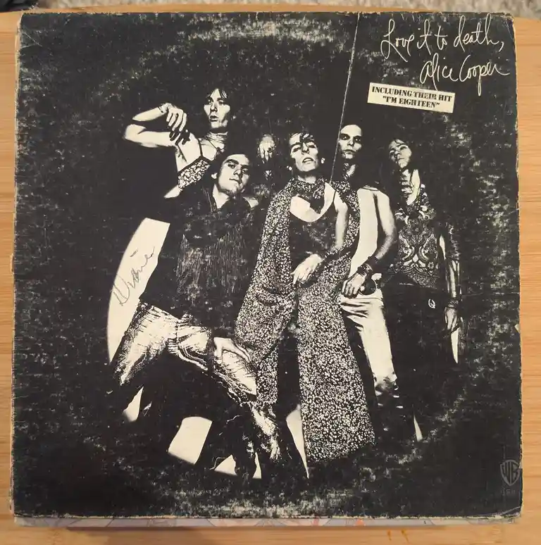A worn, black-and-white album cover for Alice Cooper's 'Love It to Death' shows the band in theatrical, dark attire. The…