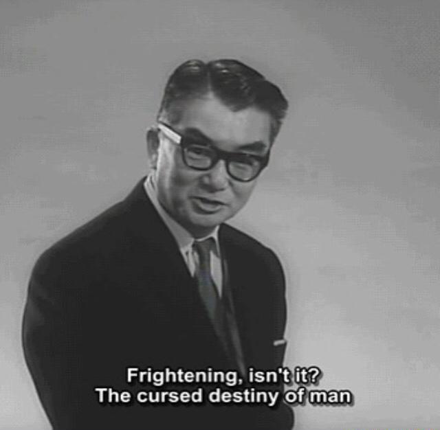 A black-and-white photo of a man in a suit and glasses looking slightly to the side with a serious expression. White text…
