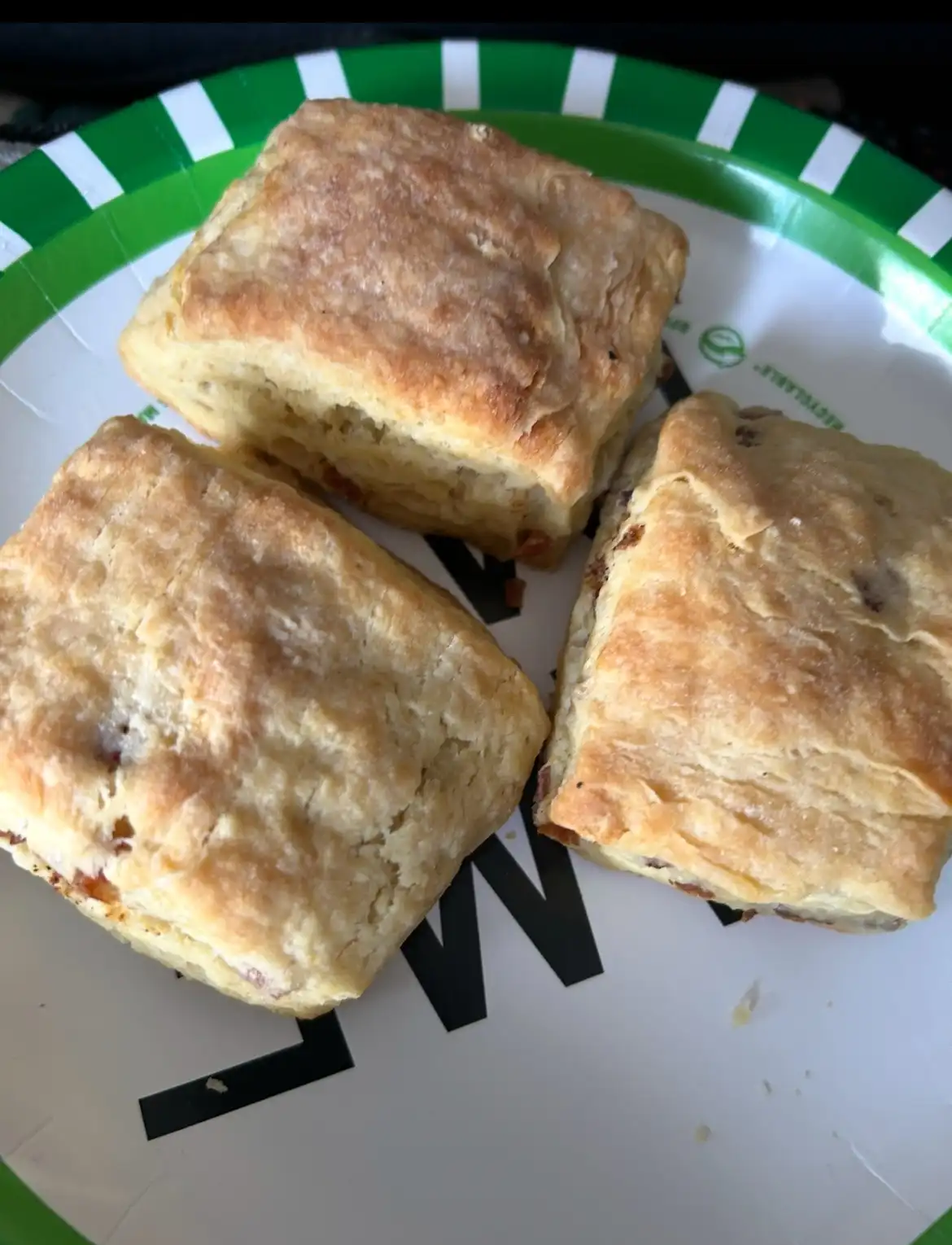 Three golden-brown, flaky square pastries sit on a green-and-white striped paper plate with partial black lettering. The…